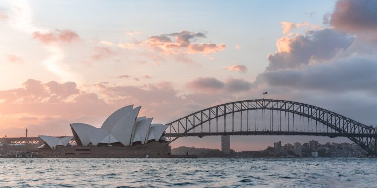 Stylish modern building and arch bridge crossing harbor against cloudy sundown sky, representing whistleblower protections in australia