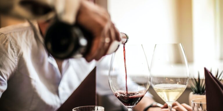 Crop man pouring red wine in glass in restaurant