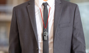 Man in suit wearing a whistle with red string, representing famous whistleblowers