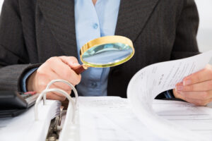 Close-up Of Businessperson Checking Bills With Magnifying Glass, representing Caremark Fraud