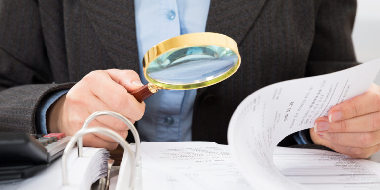 Close-up Of Businessperson Checking Bills With Magnifying Glass, representing Caremark Fraud